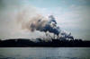 Looking across river at an industrial plant spewing toxic smoke into the sky